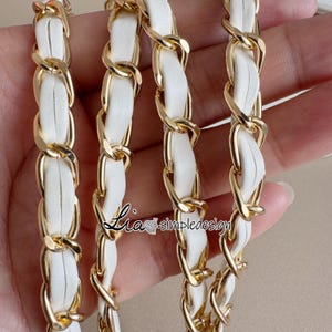 May include: Close-up of a gold chain with white leather woven through the links. The chain is a bright gold color, and the leather is a clean white. The chain is likely for a purse or handbag.
