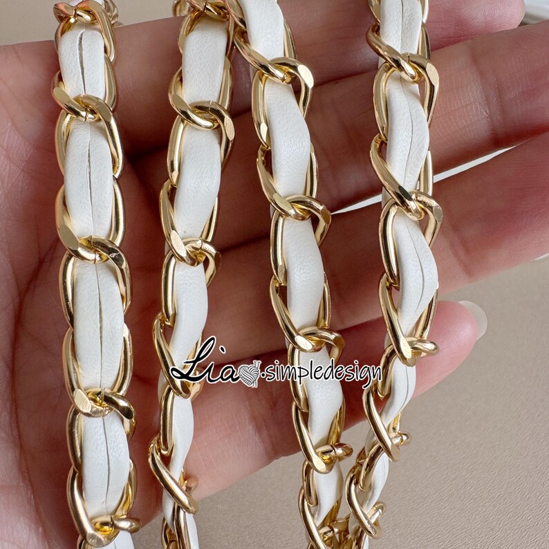 May include: Close-up of a gold chain with white leather woven through the links. The chain is a bright gold color, and the leather is a clean white. The chain is likely for a purse or handbag.