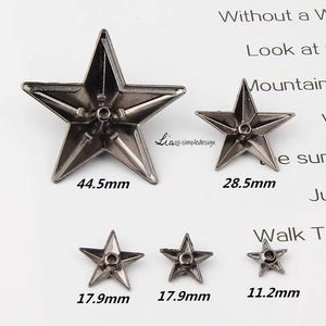 May include: Five silver metal star-shaped embellishments in various sizes. The largest star measures 44.5 mm, the next largest measures 28.5 mm, and the three smallest stars measure 17.9 mm and 11.2 mm.