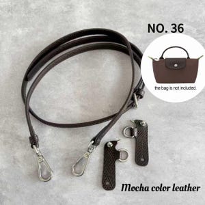 Può includere: Un cinturino per borsa in pelle color moka con chiusure e attacchi in metallo color argento. L'immagine include una piccola illustrazione di una borsa marrone e il testo "la borsa non è inclusa."