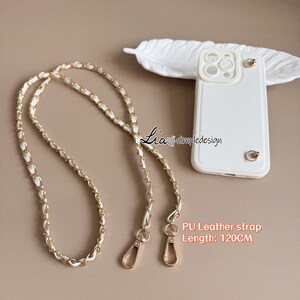 May include: White phone case with gold hardware and a detachable chain strap. The strap is white PU leather woven with gold-tone metal links. The strap is 120cm long.