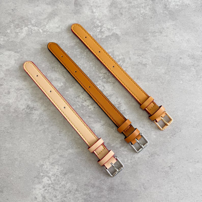 May include: Three leather watch straps in varying shades of tan and brown, each featuring a series of adjustment holes, a sliding keeper loop, and a metal buckle. The straps are arranged diagonally, showcasing a light beige, a medium tan, and a darker brown.
