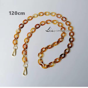 Pode incluir: Uma corrente marrom e dourada com dois fechos. A corrente tem 120 cm de comprimento.