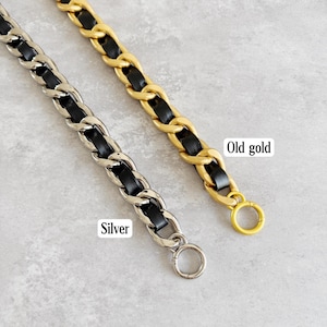 Peut inclure: Deux cha&icirc;nes m&eacute;talliques avec du cuir noir entrelac&eacute; dans les maillons. Une cha&icirc;ne est argent&eacute;e et porte l'&eacute;tiquette Silver, tandis que l'autre est dor&eacute;e et porte l'&eacute;tiquette Old gold. Chaque sangle poss&egrave;de un anneau m&eacute;tallique circulaire.