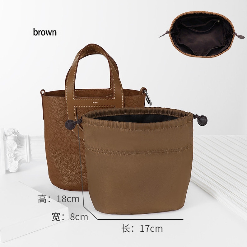 May include: Brown leather handbag with a top handle and a drawstring dust bag. The bag measures 18 cm tall, 8 cm wide, and 17 cm long.