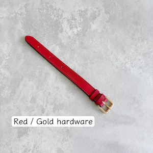 May include: A red watch strap featuring gold-toned metal hardware, including a buckle and two loops. The strap has a series of pre-punched holes for adjustment. The text "Red / Gold hardware" is printed in black on the lower portion of the image.