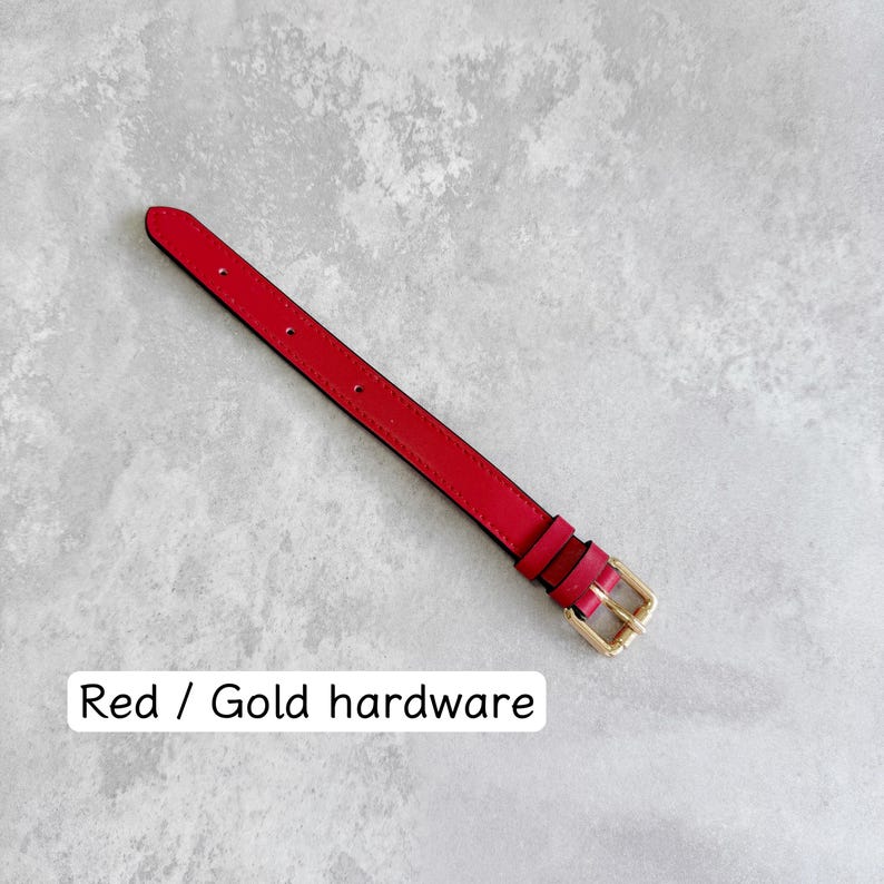 May include: A red watch strap featuring gold-toned metal hardware, including a buckle and two loops. The strap has a series of pre-punched holes for adjustment. The text "Red / Gold hardware" is printed in black on the lower portion of the image.