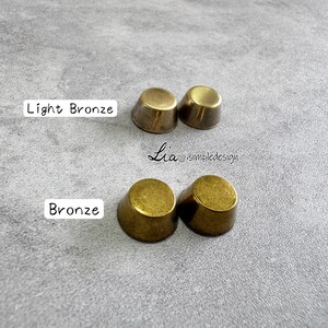 May include: Two sets of bronze-coloured thimble-shaped objects. One set is labelled "Light Bronze" and the other "Bronze". The text "Lia simpledesign" is also visible. The objects are on a grey surface.