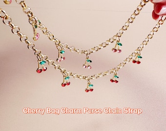 Könnte beinhalten: Goldfarbener Kettenriemen mit hängenden Kirsch-Anhängern. Jeder Kirsch-Anhänger hat rote, rosa und grüne Akzente. Der Text "Cherry Bag Charm Purse Chain Strap" ist unten im Bild zu sehen.