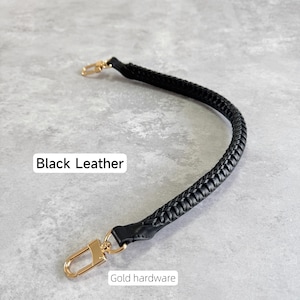 May include: A black, braided leather handbag strap with gold-coloured clasps. The text "Black Leather" and "Gold hardware" are visible. The strap is designed for easy attachment to a bag.