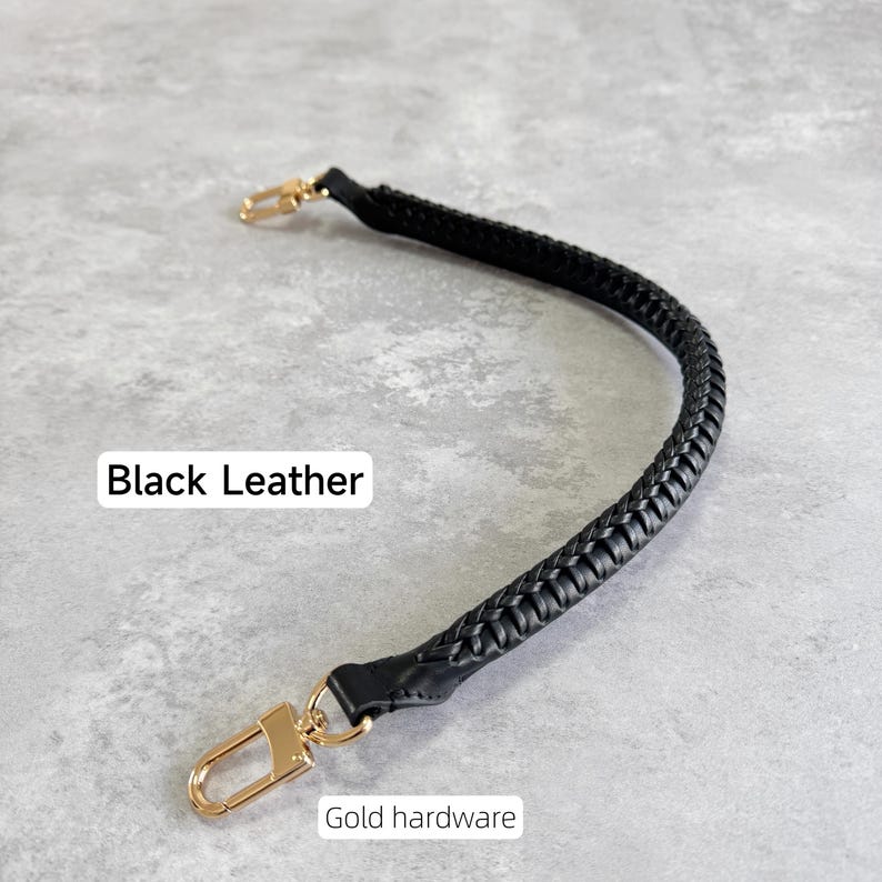 May include: A black, braided leather handbag strap with gold-coloured clasps. The text "Black Leather" and "Gold hardware" are visible. The strap is designed for easy attachment to a bag.