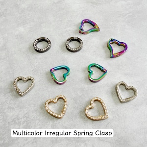 Puede incluir: Una colección de cierres de resorte irregulares en varias formas y colores. Los cierres incluyen diseños en forma de corazón y circulares, algunos con detalles de pedrería. El texto "Multicolor Irregular Spring Clasp" está en la parte inferior de la imagen.