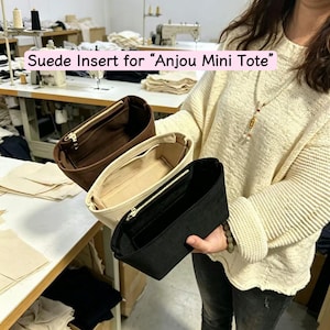 May include: Three suede inserts for the "Anjou Mini Tote" in brown, cream, and black. Each insert has a zippered top and a rectangular shape. The text "Suede Insert for "Anjou Mini Tote"" is displayed in a pink rectangle.