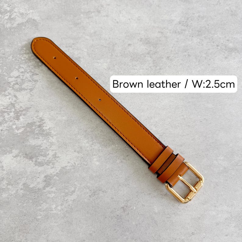 May include: A brown leather watch strap featuring gold-tone hardware, including a buckle and two keepers. The strap has visible stitching along the edges and multiple adjustment holes. The text on the image reads Brown leather / W:2.5cm.