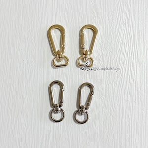 May include: Four metal clasps, two gold and two silver, with a spring-loaded gate. The clasps are designed for attaching to bags, straps, or other items.
