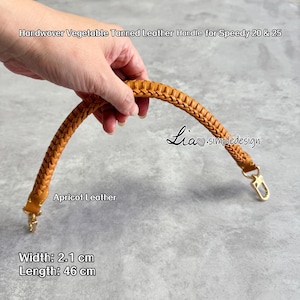 May include: Apricot-coloured handwoven vegetable-tanned leather handle for Speedy 20 & 25 bags. The handle is 2.1 cm wide and 46 cm long, featuring a braided design with gold-coloured hardware. The text "Apricot Leather" is visible.