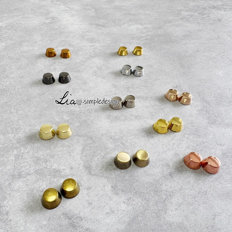 May include: A collection of metal stud earrings in different colours, such as gold, silver, bronze, and black. The earrings are displayed on a grey surface. The image includes the text "Lia simpledesign".