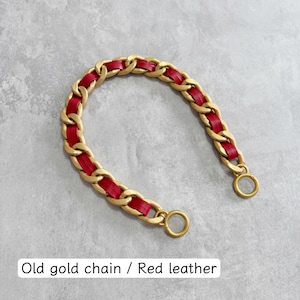 Peut inclure: Une bandouli&egrave;re incurv&eacute;e compos&eacute;e de maillons en m&eacute;tal dor&eacute; mat entrelac&eacute;s avec une bande de cuir rouge vif. La sangle se termine aux deux extr&eacute;mit&eacute;s par un anneau m&eacute;tallique dor&eacute;. Le texte indique : Old gold chain / Red leather.