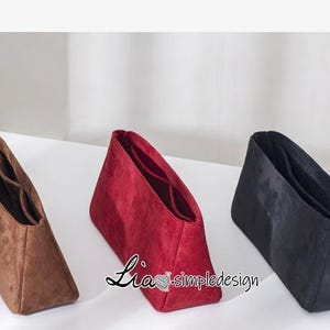 Puede incluir: Tres organizadores de bolso de ante en marrón, rojo y negro. Los organizadores tienen varios compartimentos y están diseñados para caber dentro de un bolso más grande.