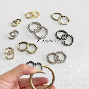 May include: Assortment of silver, gold, and black metal key rings. The key rings are in various sizes and are arranged on a white surface. Lia-simpledesign is written in the center of the image.
