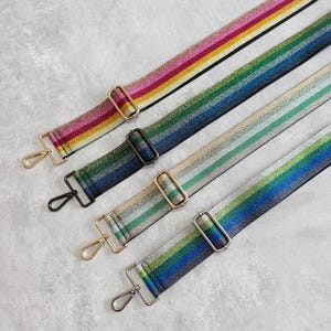 Könnte beinhalten: Vier farbenfrohe, gestreifte Taschenriemen mit metallischen Akzenten. Die Riemen weisen eine Vielzahl von Farben auf, darunter Rosa, Gelb, Grün und Blau. Jeder Riemen hat einen Metallverschluss und eine verstellbare Schnalle.