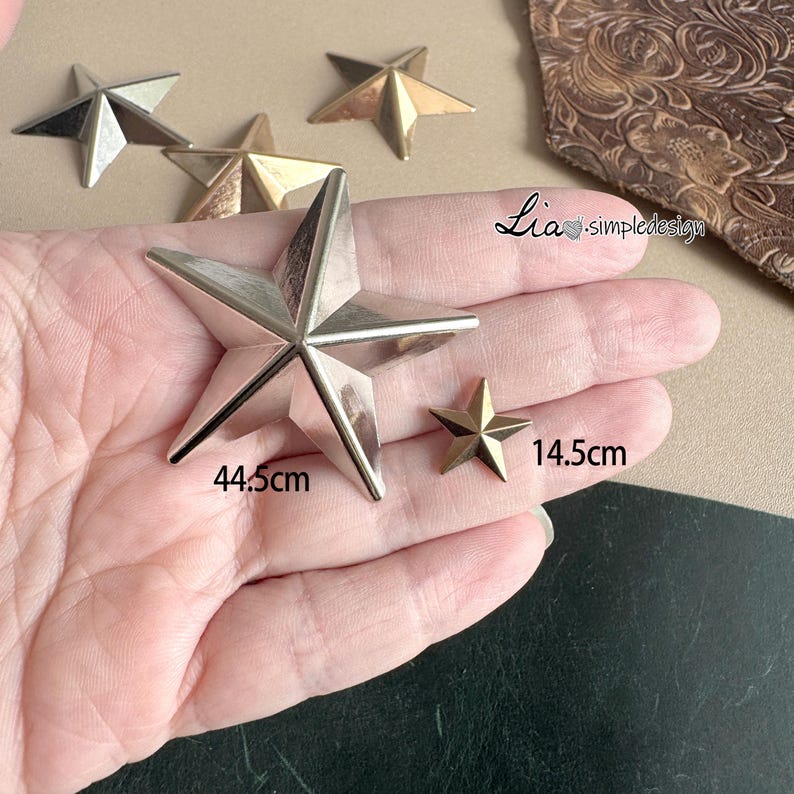 May include: Two gold-toned metal star shapes, one large and one small, are shown on a hand. The larger star is 4.5 inches wide and the smaller star is 1.5 inches wide.