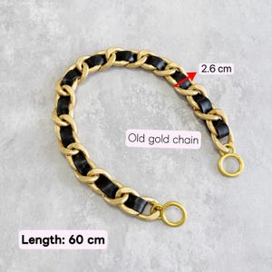 May include: An old gold chain with black leather woven through the links. The chain features a width of 2.6 cm and a total length of 60 cm, with circular clasps at both ends for attachment. The design consists of interlocking metal links.