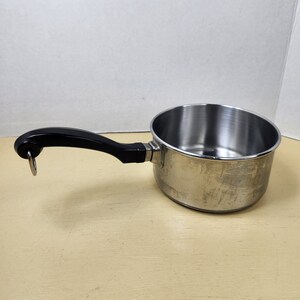 May include: A silver saucepan with a black handle. The handle has a ring on the end.
