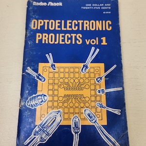 May include: A blue book with the title "Optoelectronic Projects vol 1" and the Radio Shack logo. The cover features a yellow circuit board with various electronic components, including LEDs, resistors, and a light bulb.