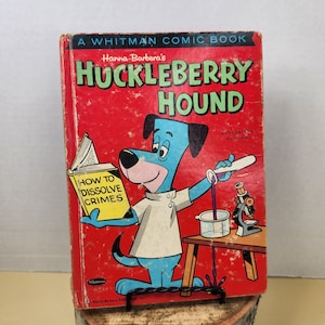 May include: Vintage Huckleberry Hound comic book. The cover is red with the title in green and the cartoon character in blue. The book is propped up on a wooden base. The book's title is "Huckleberry Hound" and the text "How to Dissolve Crimes" is visible.