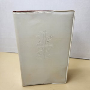 May include: White leather-bound book with a cross and the letters Alpha and Omega embossed on the front cover.