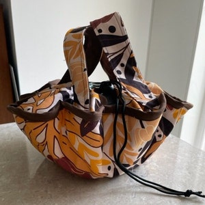 May include: A brown and white fabric bag with a drawstring closure and a floral pattern. The bag has two brown handles and a black drawstring.