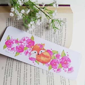 Peut inclure: Un marque-page aquarelle représentant un adorable renard orange enroulé dans des fleurs roses. Le marque-page est blanc avec une bordure rose pâle.