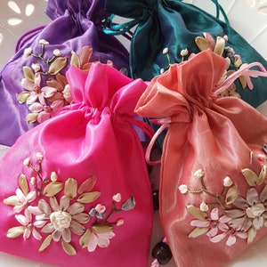 May include: Four small, colourful satin drawstring bags with embroidered floral designs. The bags are pink, purple, teal and peach.