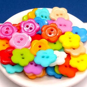 May include: Assortment of colorful plastic flower-shaped buttons with two holes each. The buttons are in various shades of pink, red, orange, yellow, green, blue, and white.