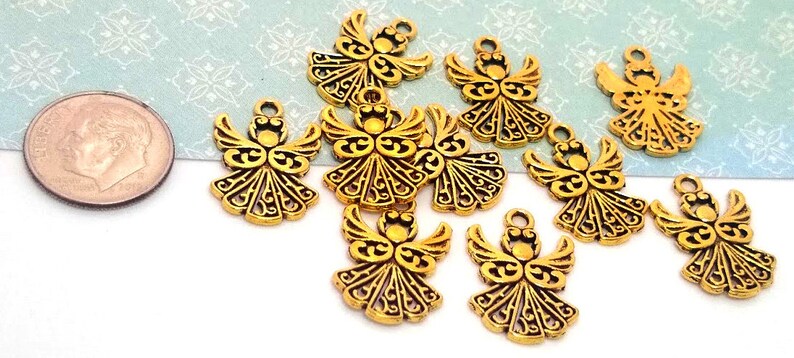 May include: Nine gold-tone metal angel charms with intricate designs. The charms are about the size of a US dime.