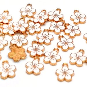May include: A collection of gold-tone metal charms featuring a white cherry blossom design. The charms have a loop at the top for attaching to jewelry or other crafts.