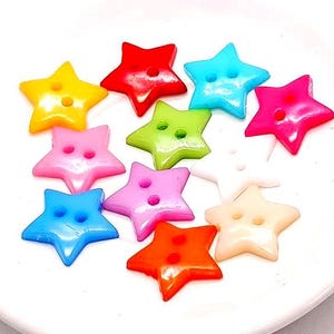 May include: A collection of colorful star-shaped buttons in various shades including yellow, red, blue, pink, green, orange, and white. Each button has two holes for sewing and is displayed on a white surface.