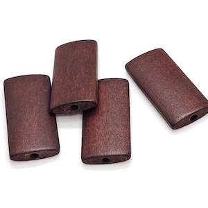 May include: Five rectangular wooden beads with rounded ends and a dark reddish-brown finish. Each bead has a small hole drilled through the centre, suggesting they are for stringing. The beads are arranged on a white background.