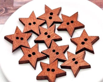 May include: A collection of eleven star-shaped buttons crafted from brown wood. Each button features a five-pointed star design with two small circular holes positioned in the centre for attachment, showcasing a visible natural wood grain texture.
