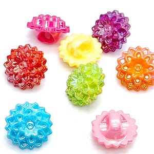 May include: Assortment of colorful plastic buttons with a flower design. The buttons are in shades of pink, purple, yellow, green, blue, and orange.