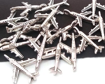 May include: A pile of silver airplane charms, scattered on a black surface. The charms are detailed and have a realistic design.