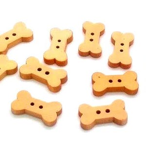 May include: A collection of light brown wooden buttons shaped like dog bones. Each button has two holes for sewing. The buttons are scattered on a white surface, ideal for craft projects or pet-themed creations.