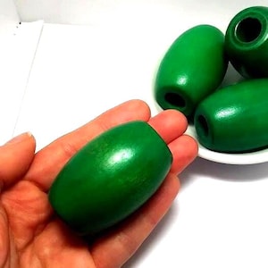 May include: A set of four smooth, barrel-shaped wooden beads with a vibrant green finish. Each bead features a central hole running through the length of the cylinder. The beads have a polished surface and a consistent, solid green color throughout.