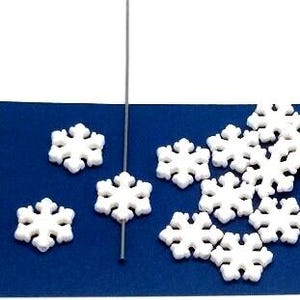 May include: White snowflake-shaped decorations scattered on a blue surface. One snowflake is attached to a thin, gray wire, and several others are scattered nearby. The snowflakes have a detailed, symmetrical design.