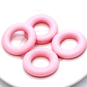 May include: Four smooth, circular rings in a solid light pink color. Each ring features a consistent rounded profile and a hollow center, arranged in a cluster. The objects have a matte finish and are uniform in their circular shape and size.