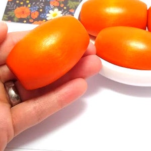 May include: Four bright orange wooden beads, oval shaped, in a white bowl and one bead in a hand.