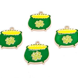May include: Four gold-coloured charms shaped like green pots of gold with yellow rims and light green shamrocks. These charms are suitable for jewellery making or other craft projects.