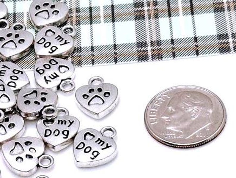 May include: Silver heart-shaped charms with the words "My Dog" and a paw print design. The charms are about the size of a US dime.