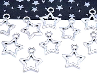 May include: A collection of silver-colored star charms with a hollow center and a small loop at the top for attaching to jewelry or crafts. The charms are arranged on a white surface with a black background decorated with white stars.